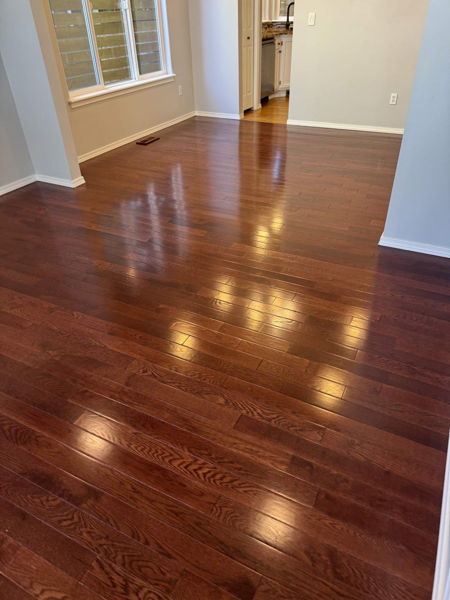 Professionally cleaned and sealed dark cherry hardwood floor in open living room, high-gloss finish reflecting natural light