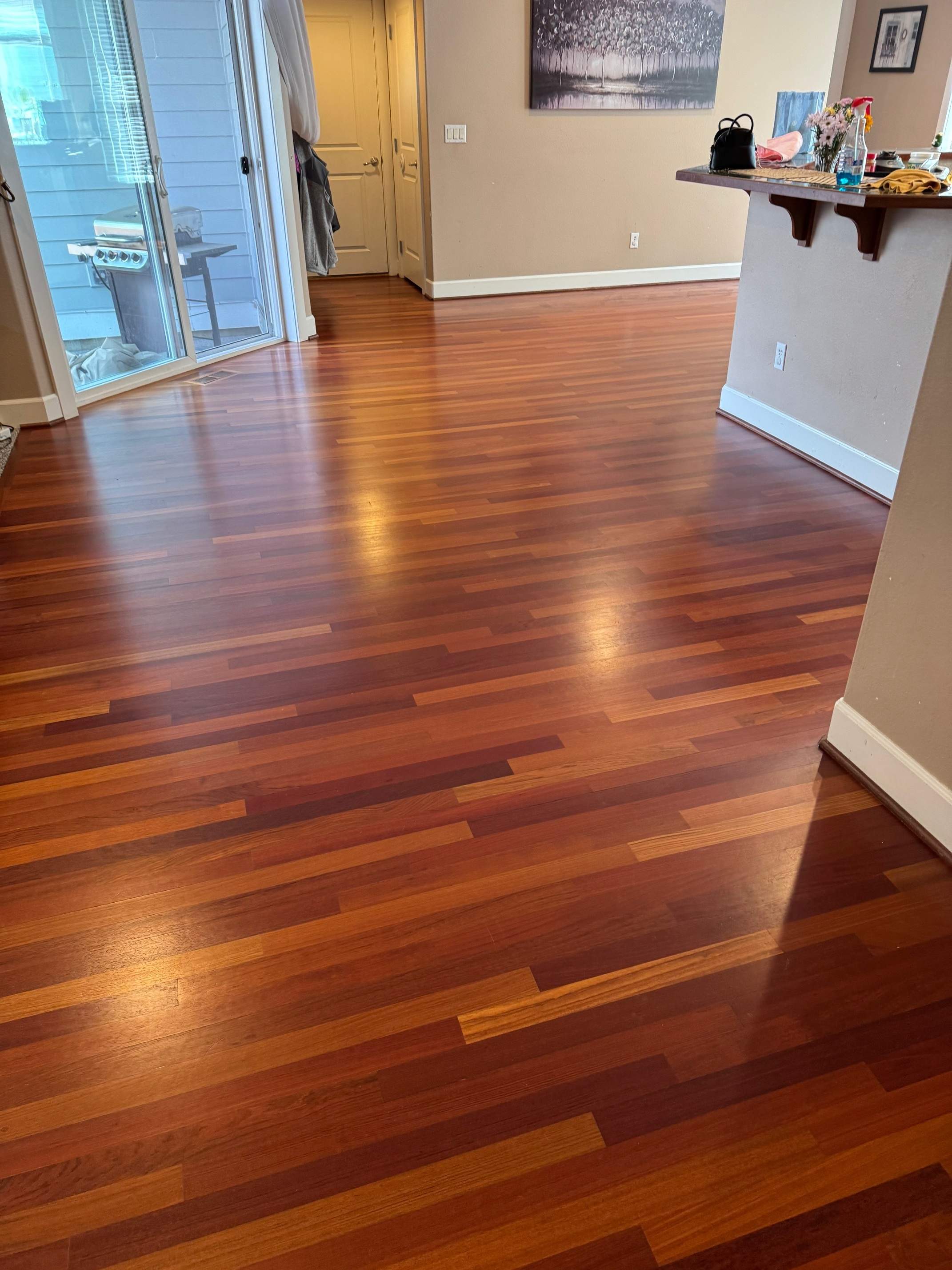 Deep red-brown exotic hardwood floor with mirror-like shine after professional cleaning and sealing near open kitchen